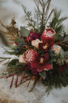 a bouquet of flowers sitting on top of snow covered ground next to plants and leaves