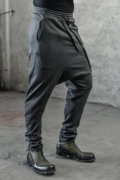 "DISTORTED ANTHRACITE DROPPED CROTCH TRACK PANTS WITH ELASTIC WAISTBAND __ELASTIC WAISTBAND WITH DRAWSTRING __J SHAPED LEGS __2 FRONT POCKETS __2 REAR BONDED POCKETS __ASYMMETRICAL HIDDEN FRONT CLOSURE model__ chest 103 (40.5\"), waist 77 (30.3\"), hips 96 (37.8\"), biceps 35 (13.8''), height 180 (5'11\"), kg 74 (163 lbs) model wears size S | color: anthracite with black matte tape fabric__ 100 cotton care__ delicate machine wash at 30 c wash inside out use cool iron do not tumble dry sizing__ s Fitted Sweatpants With Pockets, Gray Baggy Tapered Leg Pants, Fitted Tapered Leg Harem Pants With Pockets, Fitted Harem Pants With Pockets And Tapered Leg, Urban Clothing Men, Low Crotch Pants, Sporty Leggings, Winter Tights, Track Pants Mens