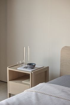 a small table with a bowl on it next to a bed