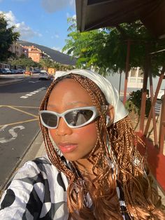 a woman with long hair wearing sunglasses and a head scarf on the side of the road