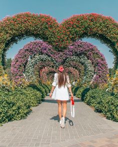 a woman walking down a walkway in front of flowers