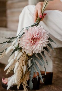 a woman holding a bouquet of flowers in her hand while sitting on the ground next to some feathers