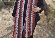 a woman wearing a red, white and black crocheted scarf standing in the desert