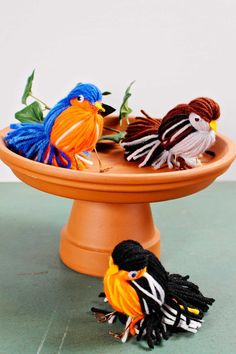 three colorful birds sitting on top of a cake plate next to another bird in the background