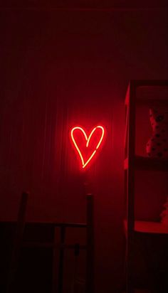 a red neon sign with a heart on it in a dark room next to a book shelf