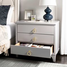 a nightstand with two drawers and a lamp on top of the night stand next to a bed