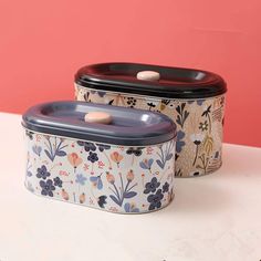 two tins sitting on top of a white table next to each other with flowers painted on them