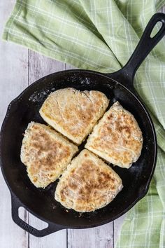 four biscuits cooking in a cast iron skillet on top of a green napkin and wooden table