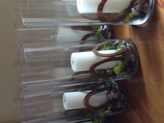 four clear glass vases with candles and rocks in them on a wooden table top