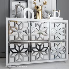 a white and gold sideboard with decorative items on it's top, in front of a mirror