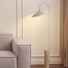 a modern floor lamp in the corner of a room next to a couch and chair