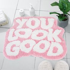 a pink rug with the words you look good on it next to slippers and a potted plant