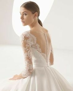 a woman in a white wedding dress with long sleeves and an open back, sitting on the floor