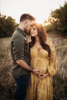 a pregnant woman and man standing in the grass at sunset with their arms around each other