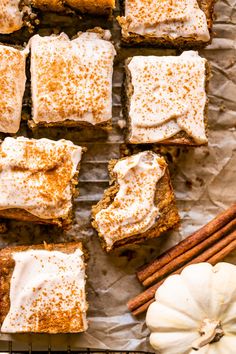 pumpkin spice bars with cinnamon sugar on top, sitting on parchment paper next to an orange pumpkin and some cinnamon sticks