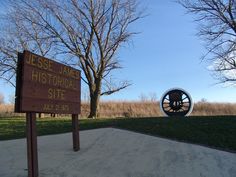 a sign in front of some trees and grass with a large tire on the ground