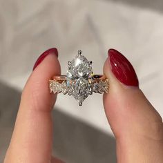 a woman's hand holding an engagement ring with two diamonds on it and a red manicure