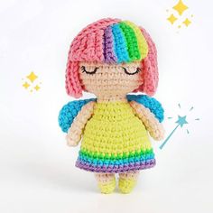 a small crocheted doll is wearing a rainbow dress and holding a sparkle wand