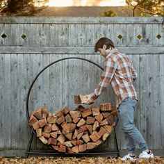 a man standing next to a pile of firewood in front of a wooden fence