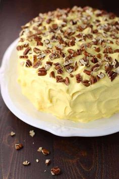 a cake on a white plate with pecans around the edges and yellow frosting