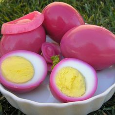 a white bowl filled with hard boiled eggs and sliced in half on top of grass