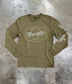 Elevate your casual wardrobe with the Wrangler Rugged Goods Long Sleeve Tee in a versatile Military Green. Designed for comfort and durability, this tee is crafted from premium, soft cotton that feels great against your skin and stands up to everyday wear. Key Features: Classic Fit: Offers a comfortable, relaxed silhouette that moves with you. Bold Sleeve Branding: Features "Wrangler" printed boldly down the sleeve, adding a touch of rugged style. Ribbed Cuffs: Ensures a snug fit around the wris Casual Outdoor Cotton Tops, Casual Cotton Tops For Outdoor, Green Cotton Tops For Outdoor, Rugged Long Sleeve Tops For Outdoor, Rugged Relaxed Fit Outdoor Top, Rugged Outdoor Relaxed Fit Top, Rugged Relaxed Fit Top For Outdoor, Rugged Relaxed Fit Tops For Fall, Cotton Graphic Tee For Outdoor