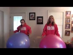 two women in red sweatshirts standing next to large exercise balls, one holding a pink and blue ball