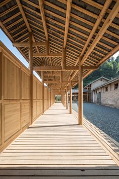 an empty wooden walkway lined with buildings in the background and trees on both sides that are covered by wood slats