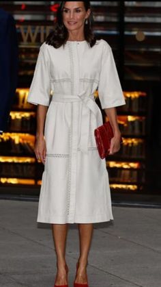 a woman in a white dress and red shoes is standing outside with her hand on her hip