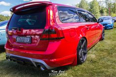 the rear end of a red car parked on top of a grass covered field next to other cars