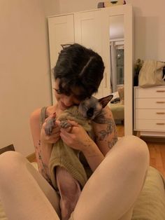 a woman sitting on the floor holding a small cat in her lap and looking at it's face