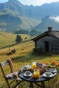 an outdoor table with breakfast on it in front of a rustic cabin and mountain range