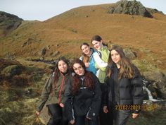 a group of young women standing next to each other on top of a grass covered hill