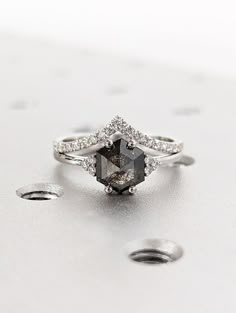 an engagement ring with a black diamond surrounded by smaller white diamonds on a silver surface