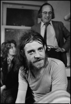 a black and white photo of a man with long hair sitting in front of other people