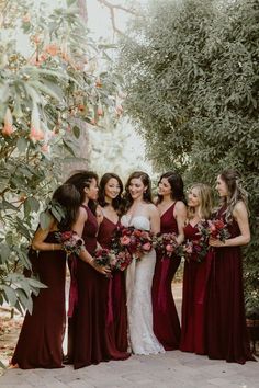 a group of women standing next to each other in front of trees and flowers on the ground