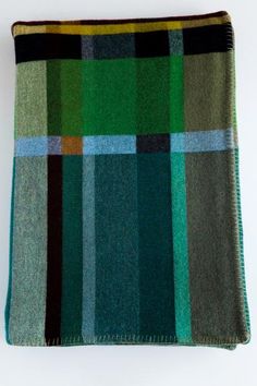 a green and black checkered blanket on a white surface with a brown border around it