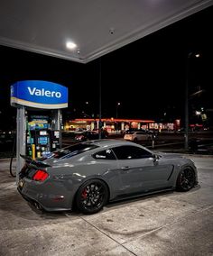 a gray sports car parked in front of a gas station at night with the word valero written on it