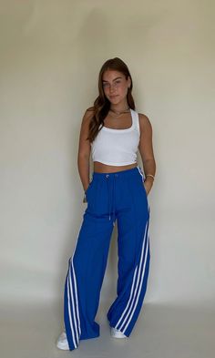 Step out with this edgy look for gamedays this fall! These blue track pants with side slits are the ultimate cool girl pant for Caturdays. So cute with chunky sneakers, or even heels for an elevated look. White stripes down the side & drawstring waist. Model is 5'5" with a 34 bust, 26" waist, 32" hips, and wearing a small. Model typically wears a 4. This item runs true to size. Pants With Side Slits, Gameday Fits, Blue Track Pants, College Gameday Outfits, Gameday Outfits, College Gameday, Blue Game, Platform Heels Boots, Blue Bodysuit