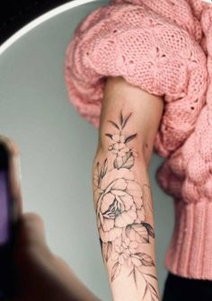 a woman with a flower tattoo on her arm taking a selfie in front of a mirror