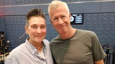 an older man standing next to a younger woman in front of a recording studio wall