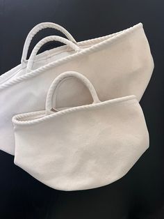 two white purses sitting next to each other on a black surface with one bag in the middle