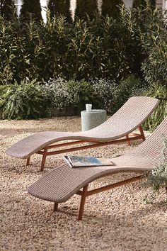 two chaise lounge chairs sitting on gravel in front of trees and bushes with potted plants