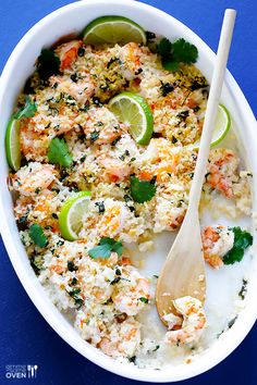 a white bowl filled with shrimp and rice next to a wooden spoon on a blue surface