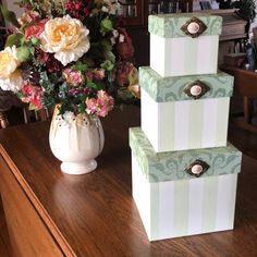 three stacked boxes sitting on top of a wooden table next to a vase with flowers