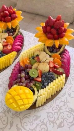 two trays filled with fruit and vegetables on top of a white cloth covered table