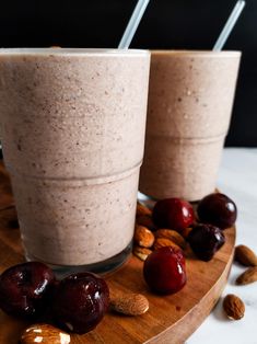 two cups filled with smoothie next to almonds and cherries