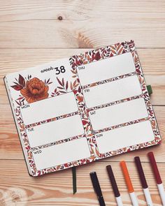 an open planner with markers and pens next to it on a wooden surface, surrounded by other stationery items