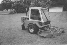 an old photo of a small tractor in the middle of a yard with trees behind it