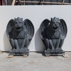 two gargoyle statues sitting next to each other in front of a white wall